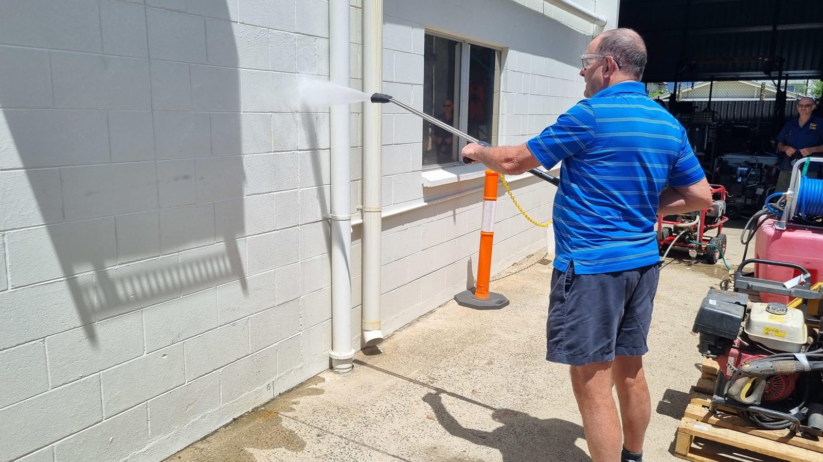 Man testing a pressure cleaner wand on a white block wall beside petrol pressure washers